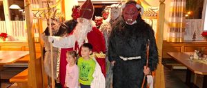 Mehrere Personen sind in Kostümen gekleidet, möglicherweise für eine Halloween-Veranstaltung. Eine Person in einem Weihnachtsmann-Kostüm steht neben zwei Kindern. Eine andere Person in einem Dämonenkostüm steht hinter ihnen.