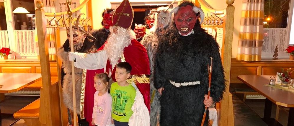 Mehrere Personen sind in Kostümen gekleidet, möglicherweise für eine Halloween-Veranstaltung. Eine Person in einem Weihnachtsmann-Kostüm steht neben zwei Kindern. Eine andere Person in einem Dämonenkostüm steht hinter ihnen.