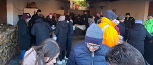 Eine Gruppe von Menschen in Winterkleidung steht in einem Raum, wahrscheinlich zur Feier eines Geburtstags. Ein Banner mit der Zahl '50' hängt an der Wand.