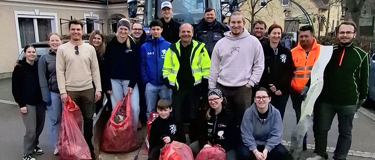 Eine Gruppe von Menschen steht draußen, einige tragen Sicherheitswesten, neben einem Traktor und Säcken mit gesammelten Gegenständen. Sie posieren für ein Foto.