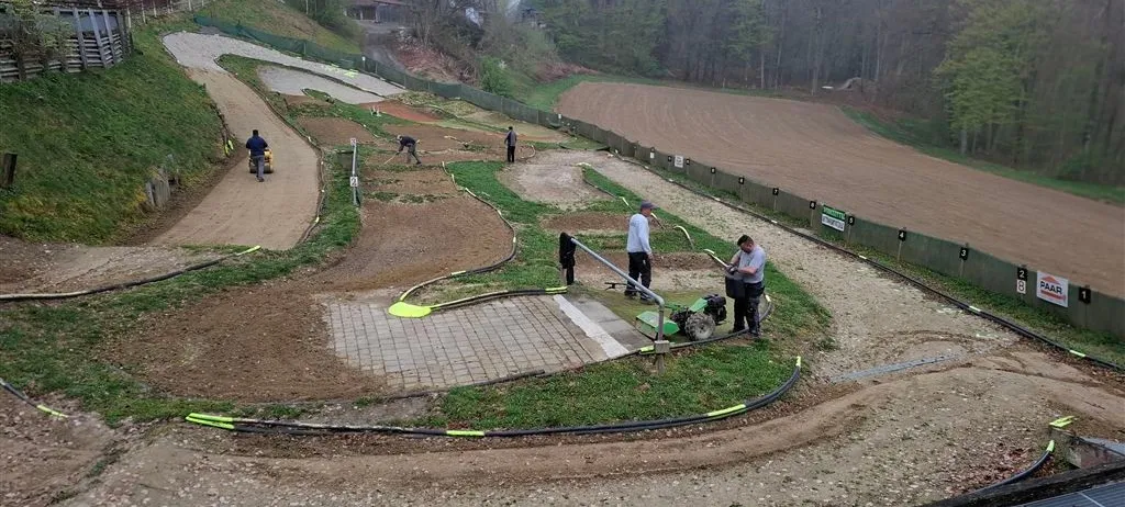 Eine Dirtbike-Strecke mit arbeitenden Personen, einer, der ein Fahrrad fährt, und anderen, die stehen und Werkzeuge halten.