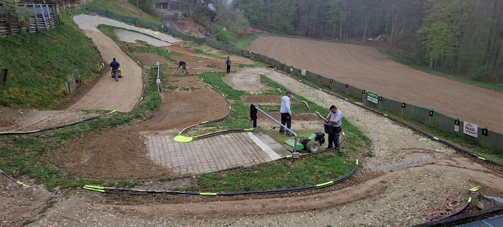 Eine Dirtbike-Strecke mit arbeitenden Personen, einer, der ein Fahrrad fährt, und anderen, die stehen und Werkzeuge halten.