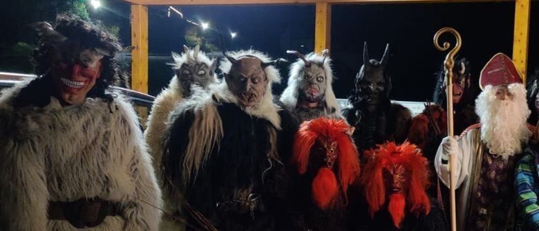 Eine Gruppe von Menschen in Kostümen, einschließlich Hörnern und Masken, posiert für ein Foto bei Nacht. Einige tragen Pelzmäntel, und einer hält einen Stab.