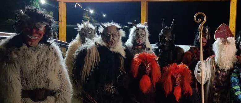 Eine Gruppe von Menschen in Kostümen, einschließlich Hörnern und Masken, posiert für ein Foto bei Nacht. Einige tragen Pelzmäntel, und einer hält einen Stab.