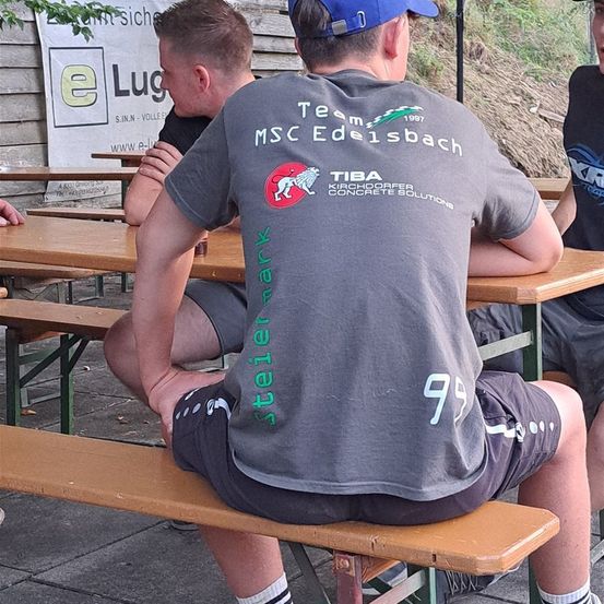 Bild enthält, T-Shirt, Person, Sitting, Baseball Cap, Cap, Hat, Wood, Bench, Furniture, Face