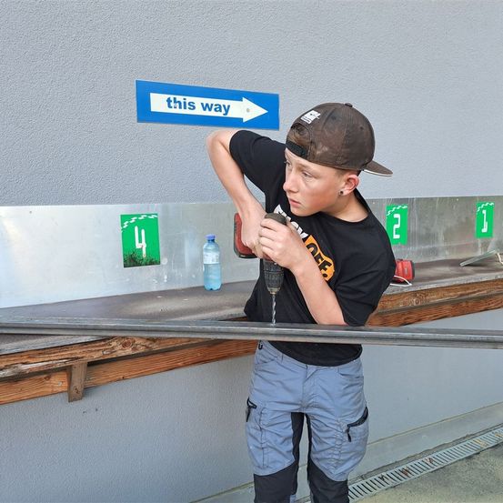 Bild enthält, Person, Worker, Furniture, Table, Device, Power Drill, Tool, Baseball Cap, Clothing, Hat