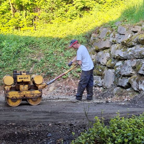 Ein Mann benutzt einen gelben Walzenzug, um die Straße zu ebnen, während er einen Hut und Handschuhe trägt.