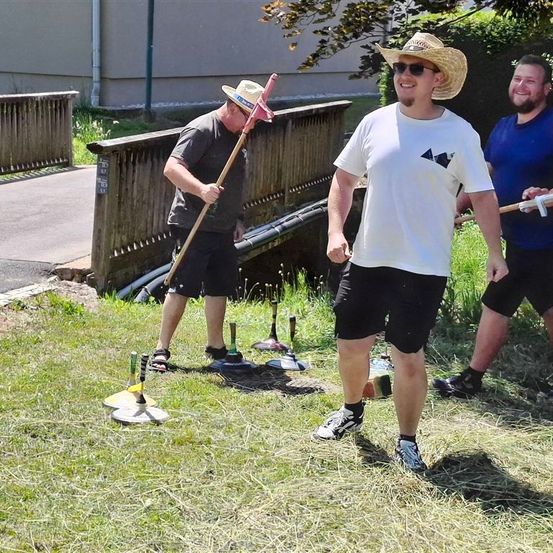 Drei Männer spielen ein Spiel Croquet auf einer Rasenfläche. Ein Mann hält einen Schläger, während ein anderer Mann ihn ansieht.