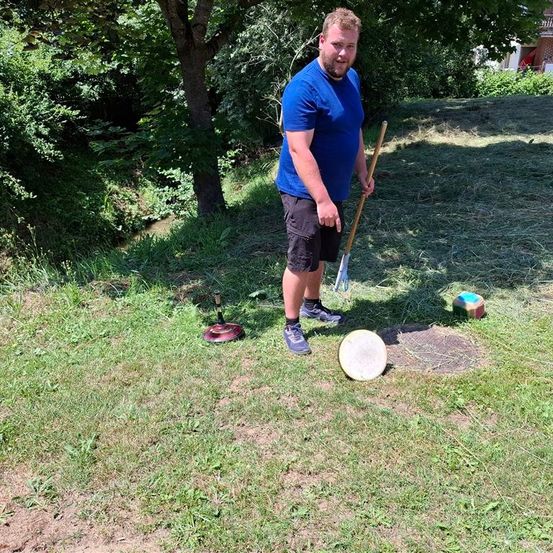 Ein Mann in einem blauen T-Shirt hält einen Stock und schaut ein Frisbee auf einem Grasfeld an.