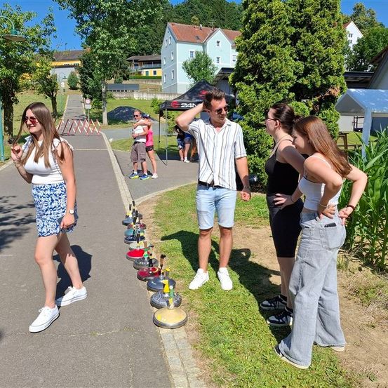Eine Gruppe von Menschen steht an einem sonnigen Tag im Freien. Sie sind in einem Park mit einer Reihe von Hütchen auf dem Gras.