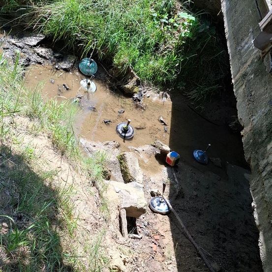 Ein schlammiger Bereich mit etwas grünem Gras und Pflanzen, mit mehreren Metallgegenständen, die herumliegen, einige teilweise im Schlamm eingesunken.