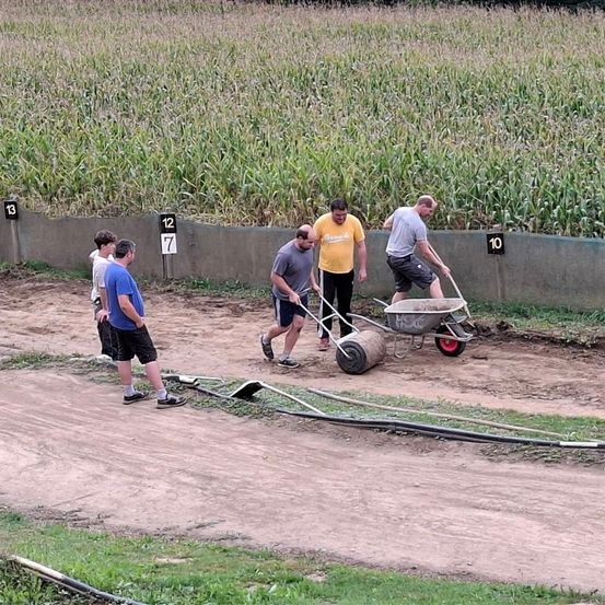 Fünf Männer arbeiten auf einer Erdbahn mit den Nummern 7, 12 und 13 an der Wand. Ein Mann schiebt einen Schubkarren, während ein anderer neben ihm steht.