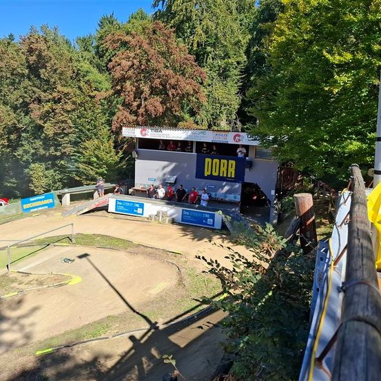 Ein Freiluftbereich mit einer Erdstrecke und einem Gebäude namens 'DORR', von dem aus Zuschauer die Strecke beobachten.