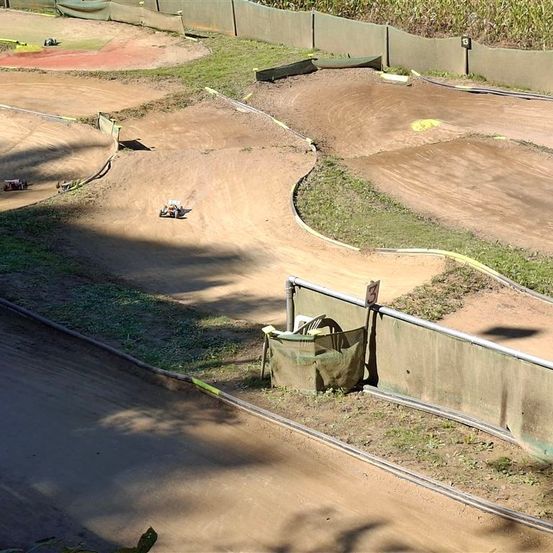 Eine Erdrennstrecke mit mehreren fahrenden Fahrzeugen. Die Strecke hat Kurven und Geraden, umgeben von grünem Gras und Betonbarrieren.