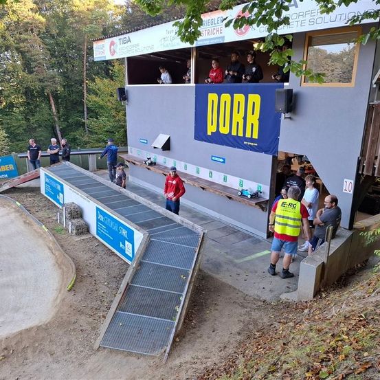 Ein Gebäude mit dem Wort Dorr darauf hat Menschen, die eine Outdoor-Veranstaltung beobachten. Einige Leute stehen auf den Stufen und eine Person trägt eine gelbe Weste.