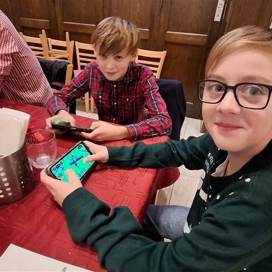 Zwei junge Jungen spielen ein Spiel auf ihren Handys an einem Restauranttisch, mit einem Korb voller Servietten und einem Glas in der Nähe.