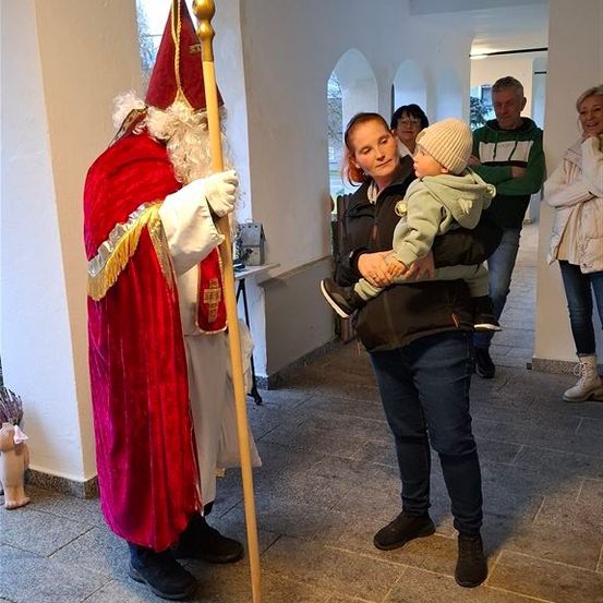 Eine Frau hält ein Baby, während ein Mann als Weihnachtsmann verkleidet neben ihr steht, während eine andere Frau und ein Mann dahinter gehen.