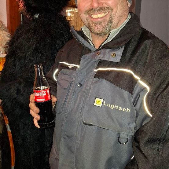 Ein lächelnder Mann hält eine Coca-Cola-Flasche in der Hand, neben einer bärenartigen Figur.