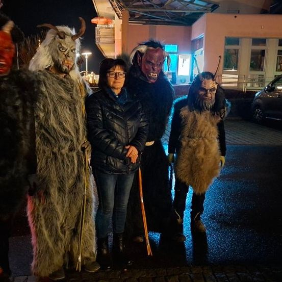 Fünf Menschen posieren nachts für ein Foto. Einer trägt eine schwarze Jacke und Jeans. Die anderen sind in pelzigen Kostümen. Dahinter steht ein Gebäude mit Lichtern.