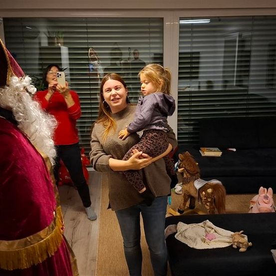 Ein Familienfoto mit dem Weihnachtsmann in einem Wohnzimmer mit einer Couch, Spielzeug und einer Frau, die mit ihrem Handy ein Foto macht.