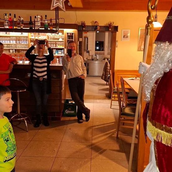 Menschen machen Fotos in einem Restaurant. Eine Person in einer Weihnachtsmann-Kostüm steht neben dem Tisch. Einige Leute sitzen und andere stehen.