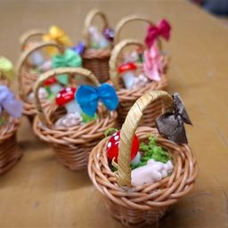 Mehrere kleine dekorative Weidenkörbchen mit bunten Schleifen und verspielten Pilzfiguren stehen auf einem Holztisch.