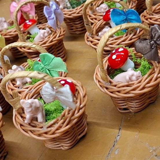 Mehrere kleine Korbe aus Weide mit Moos, kleinen Spielzeugen und bunten Bändern stehen auf einer Holzoberfläche. Jeder Korb enthält einzigartige Figuren und Dekorationen.