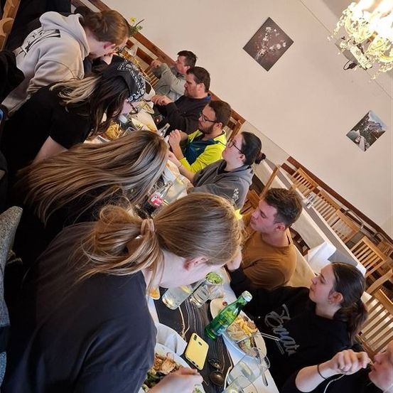 Eine Gruppe von Menschen sitzt an einem Tisch in einem Restaurant mit Essen und Getränken auf dem Tisch.