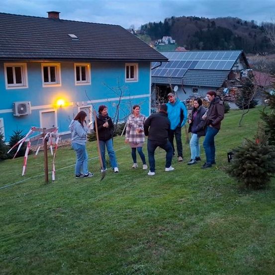 Eine Gruppe von Menschen steht vor einem blauen Haus und hält Schaufeln in der Hand, vor einem Weihnachtsbaum.