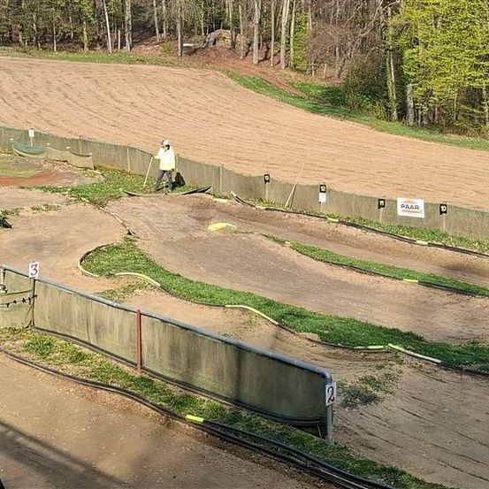 Eine Person bereitet eine Dirt-Rennstrecke mit Barrieren, markierten Nummern und Bäumen im Hintergrund vor.