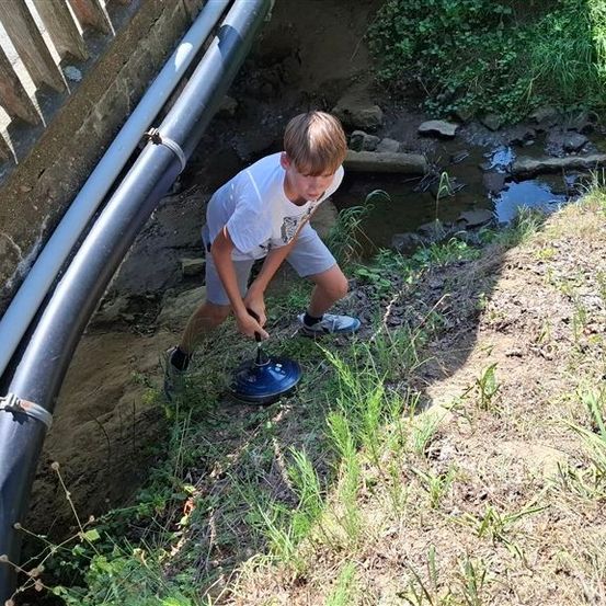 Ein junger Junge benutzt ein blaues Gerät, um in der Nähe eines kleinen Baches in den Boden zu graben.