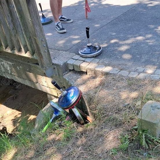 Eine Person steht auf einem Bürgersteig in der Nähe eines Holzzauns, mit mehreren blauen und silbernen Objekten, die in der Nähe im Boden vergraben sind.