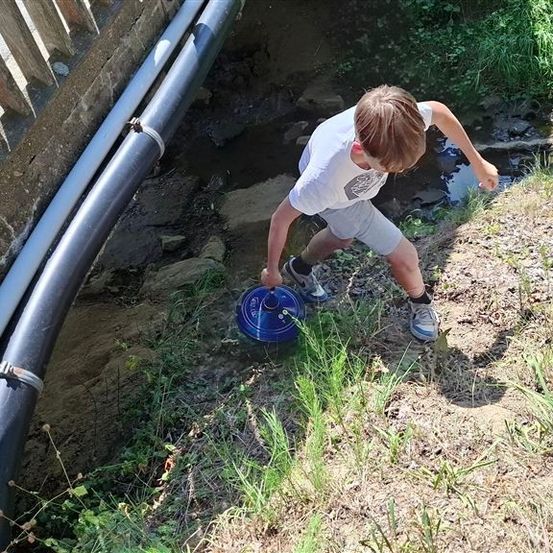 Ein junger Junge beugt sich über einen kleinen Bach und hält ein blaues Objekt in der Hand.