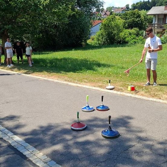 Eine Gruppe von Menschen spielt auf einer Straße ein Spiel Beer Pong mit einem Grasfeld im Hintergrund.