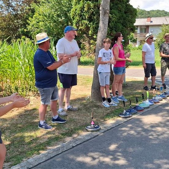 Eine Gruppe von Menschen steht auf einem Bürgersteig mit einer Reihe aufgestellter Bowling-Pins. Sie sind lässig gekleidet und scheinen in ein Gespräch vertieft zu sein.