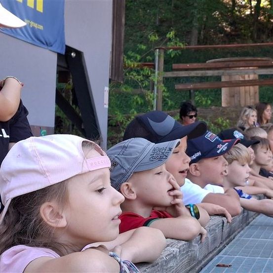 Eine Gruppe von Kindern mit Mützen sitzt auf einer Bank und schaut etwas vor sich an.