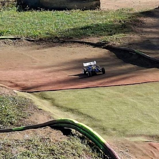 Ein kleines ferngesteuertes Auto fährt auf einer Erdstrecke mit einem nahegelegenen Grasbereich.