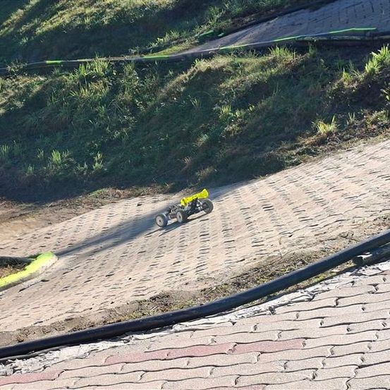Ein kleines gelbes Spielzeugauto fährt auf einer gepflasterten Straße mit einem schiefen Grasbereich an der Seite.