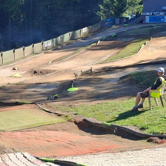 Ein Mann in einer gelben Weste sitzt auf einem Stuhl auf einer Dirtbike-Strecke, mit einem kleinen Fahrzeug auf der Strecke.