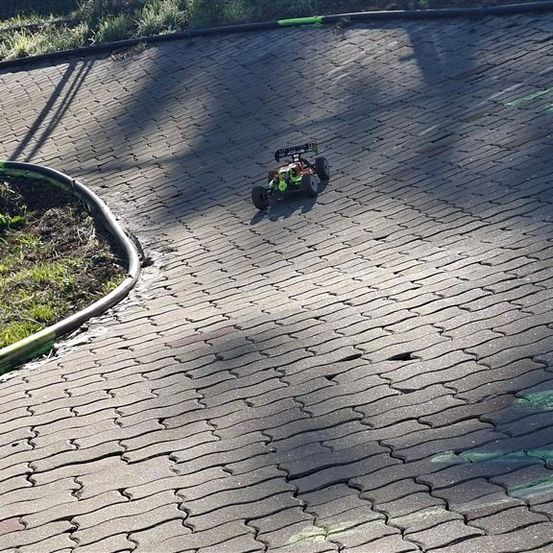 Ein ferngesteuertes Auto fährt auf einer kurvenreichen Ziegelstraße mit grünen Markierungen.