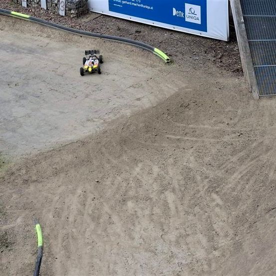 Ein ferngesteuertes Auto fährt auf einer Erdstrecke mit einem blauen Banner und Solarmodulen im Hintergrund.