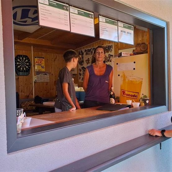 Eine Frau und ein Junge stehen an einer Theke in einer Bar, mit einer Frau, die vor dem Fenster steht.