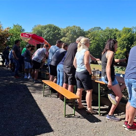 Eine Gruppe von Menschen wartet an einem Essensstand an einem sonnigen Tag.