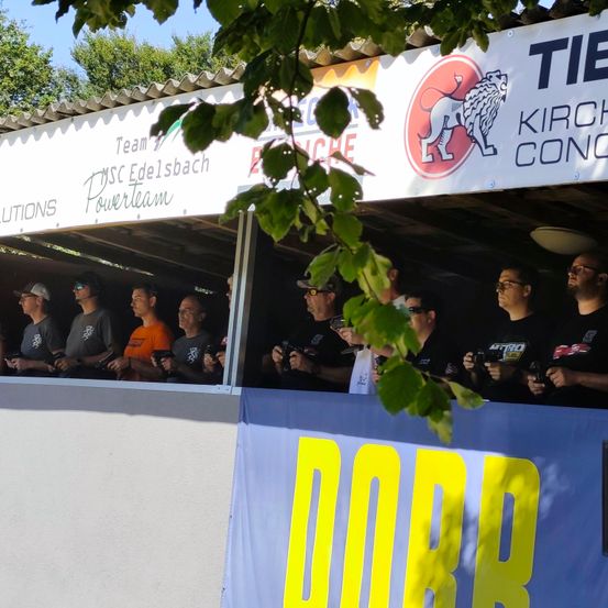 Eine Gruppe von Menschen in einer Kabine mit einem Banner, auf dem 'DORB' steht. Sie halten Kameras und scheinen Fotos zu machen.