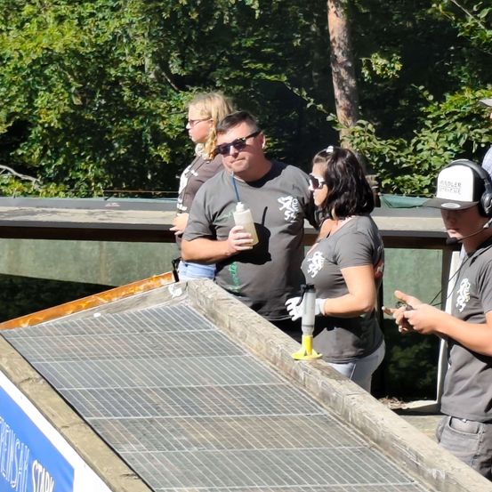 Eine Gruppe von Menschen steht auf einer Brücke mit einem Solarpanel. Ein Mann hält eine Flasche.
