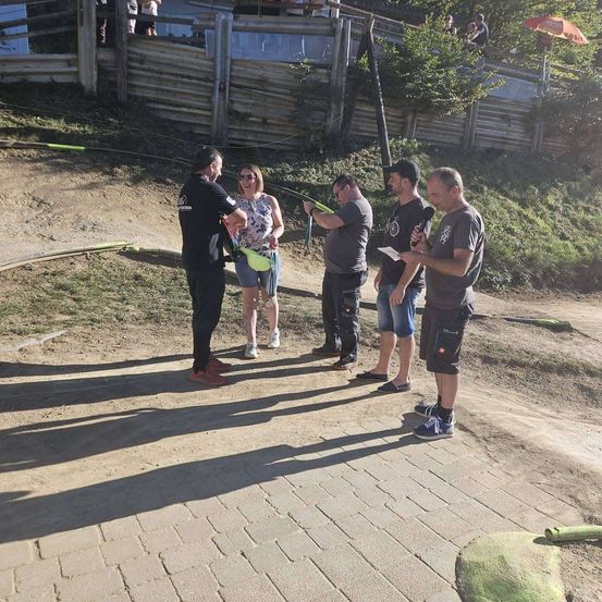 Eine Gruppe von Menschen steht auf einem Lehmweg, einer Mann hält ein Mikrofon und ein anderer ein Stück Papier. Sie tragen alle Freizeitkleidung.