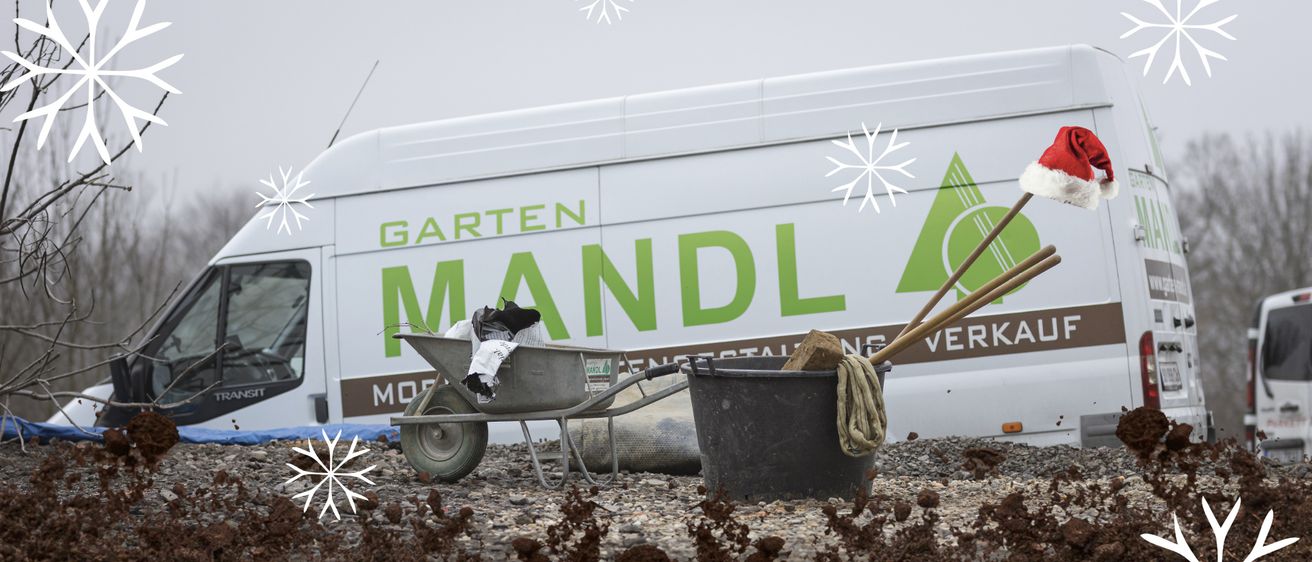 Ein weißer Lieferwagen mit der Aufschrift Garten Mandl steht mit einem Schubkarren und einem Eimer auf einer Kiesfläche. Auf dem Bild sind Schneeflocken.