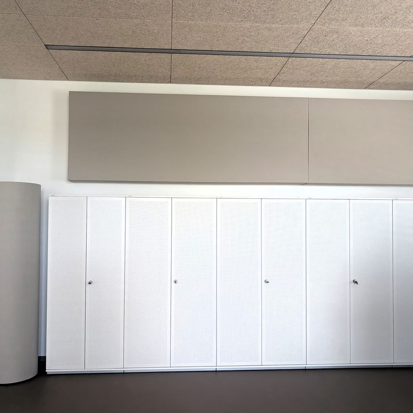 Ein leerer Raum mit einer Reihe weißer Schränke, einer grauen Platte an der Wand und einem grauen zylindrischen Objekt auf der linken Seite.