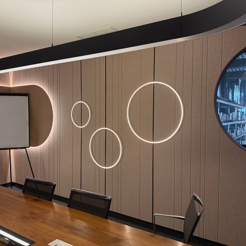 Ein moderner Konferenzraum mit einem Holztisch, kreisförmigen Beleuchtungskörpern und einem großen Fenster mit Blick auf eine Stadt.