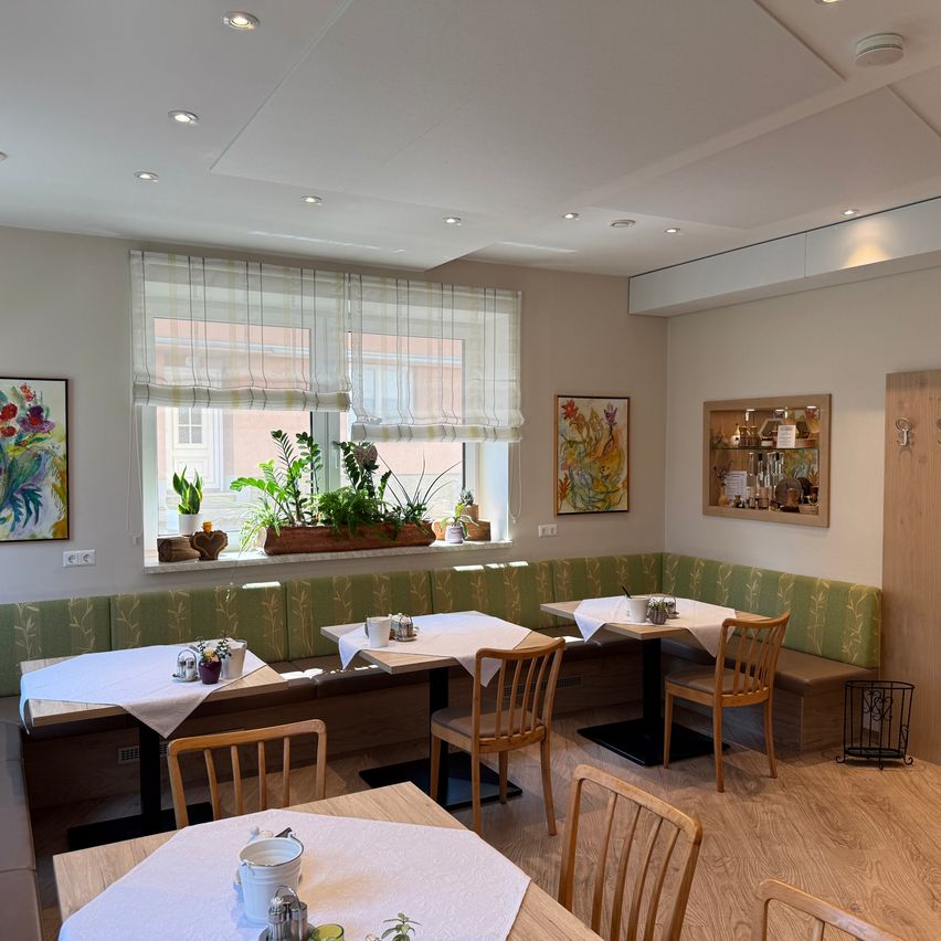 Ein Innenrestaurant mit Holztischen und Stühlen, einem Fenster mit Pflanzen und Kunstwerken an den Wänden.